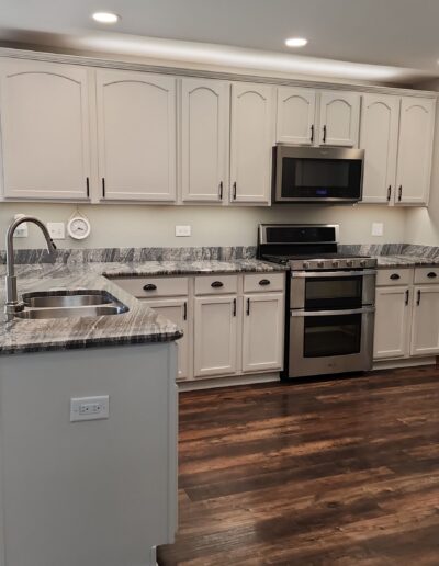 A white kitchen with stainless steel appliances and hardwood floors.