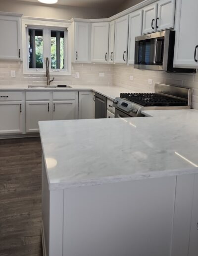 A kitchen with white cabinets and marble counter tops.