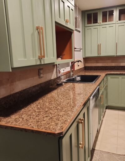 A kitchen with green cabinets and granite counter tops.