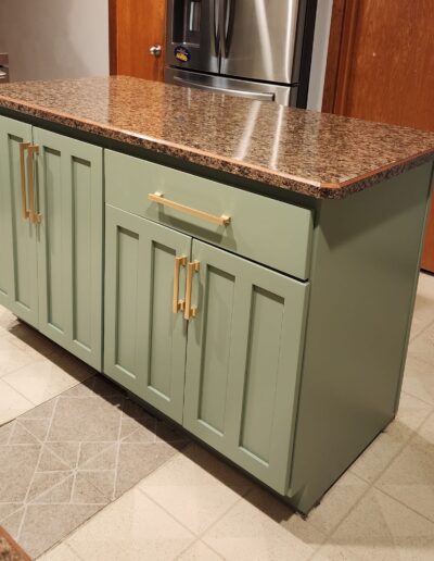 A kitchen island with green cabinets and granite counter tops.