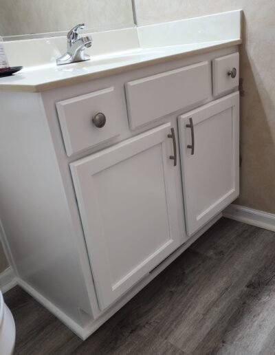 A bathroom with white cabinets and wood floors.