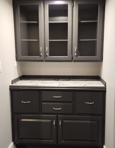 A kitchen with gray cabinets and marble counter tops.