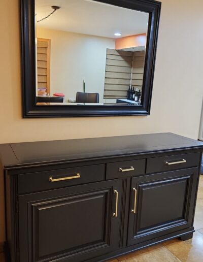 A black sideboard with a mirror in front of it.